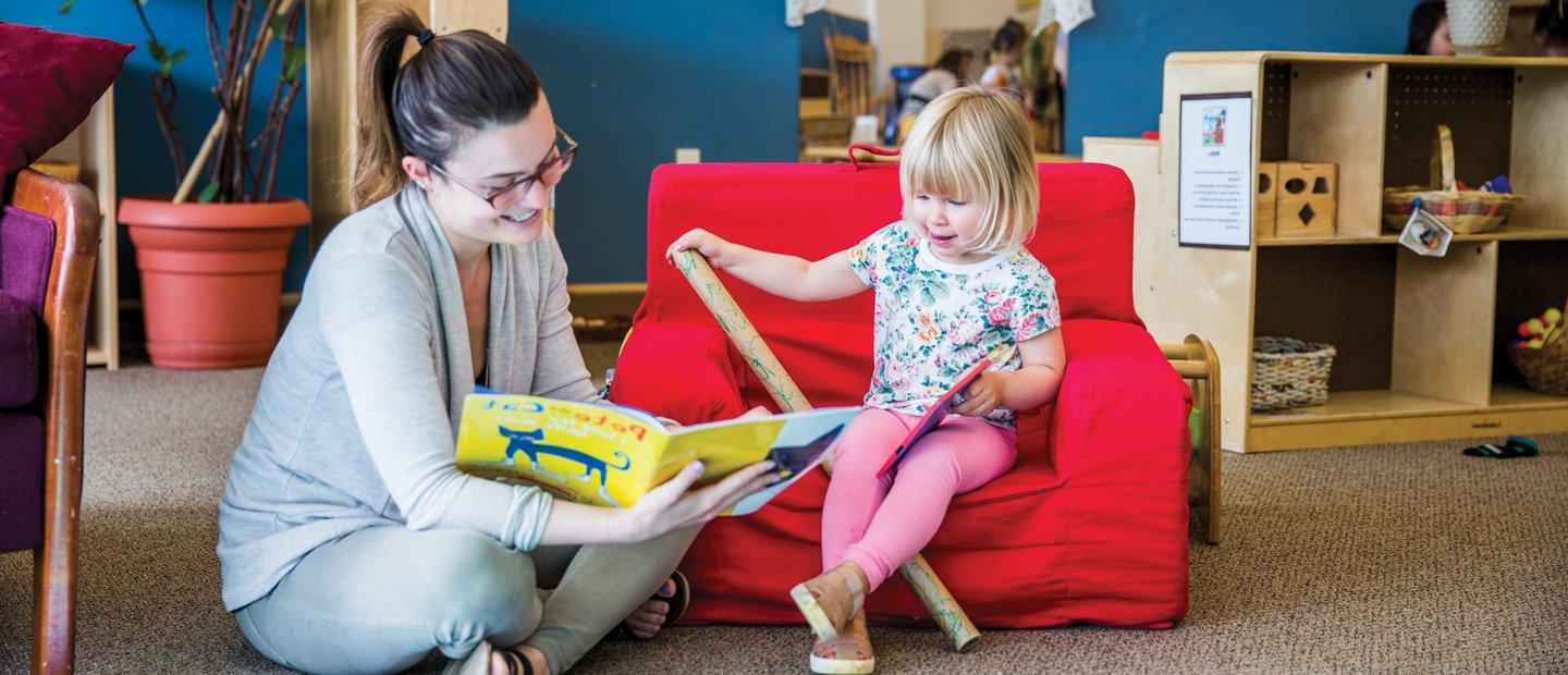 Woman reading book to child sitting on a chair